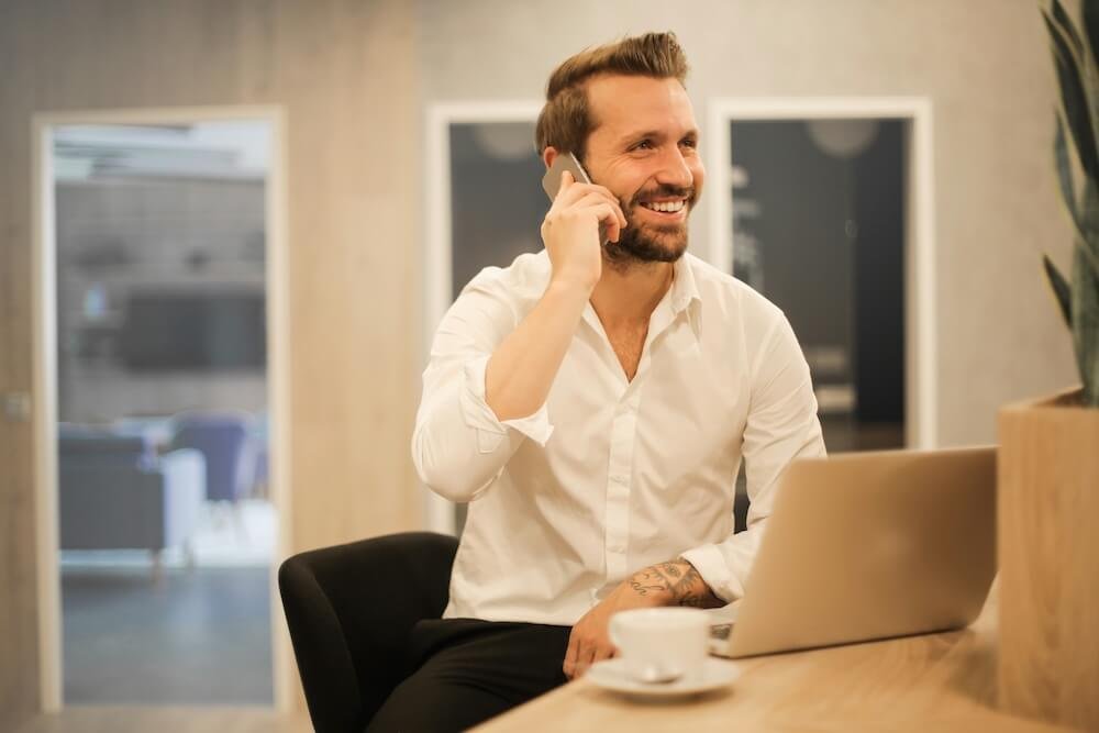 Man taking a mobile phone call beside a laptop and coffee at a table